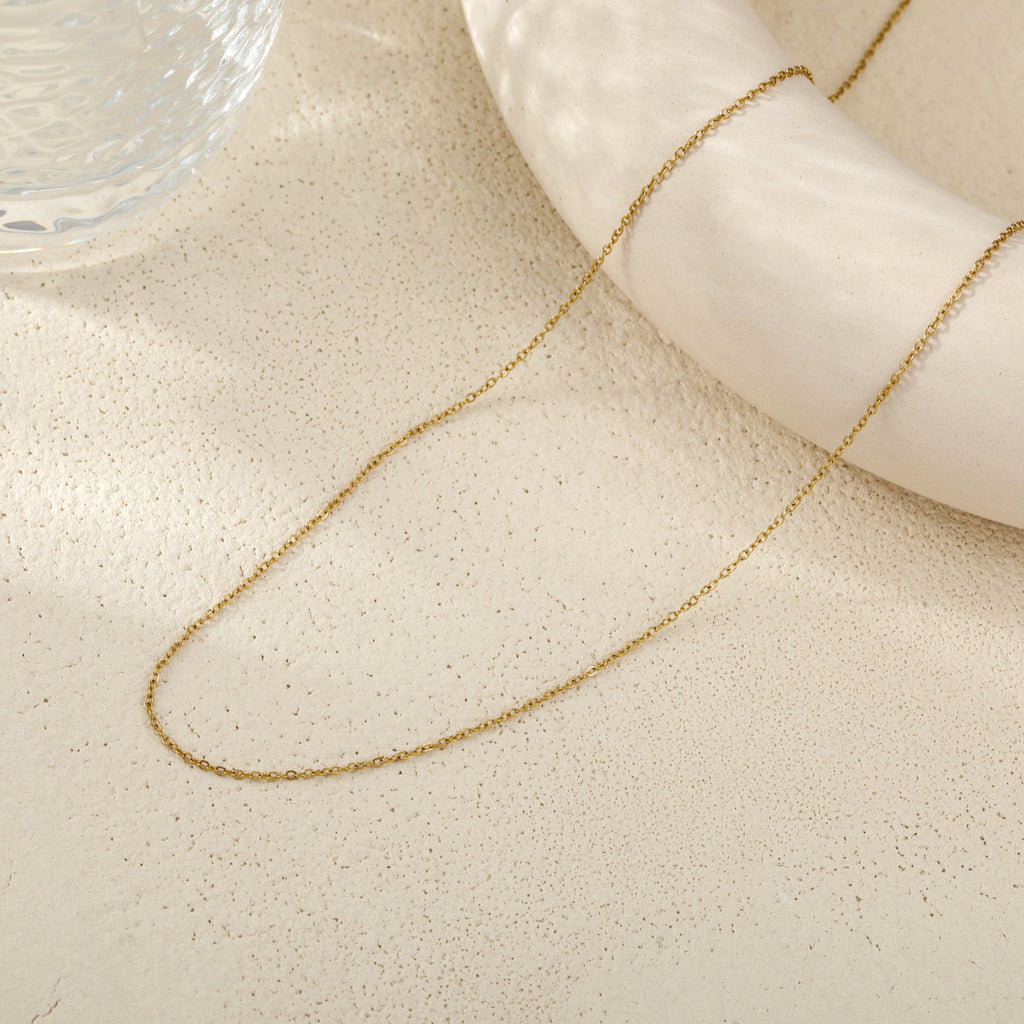 A delicate gold chain necklace draped over a white nautical-style ring prop on a textured beige surface.