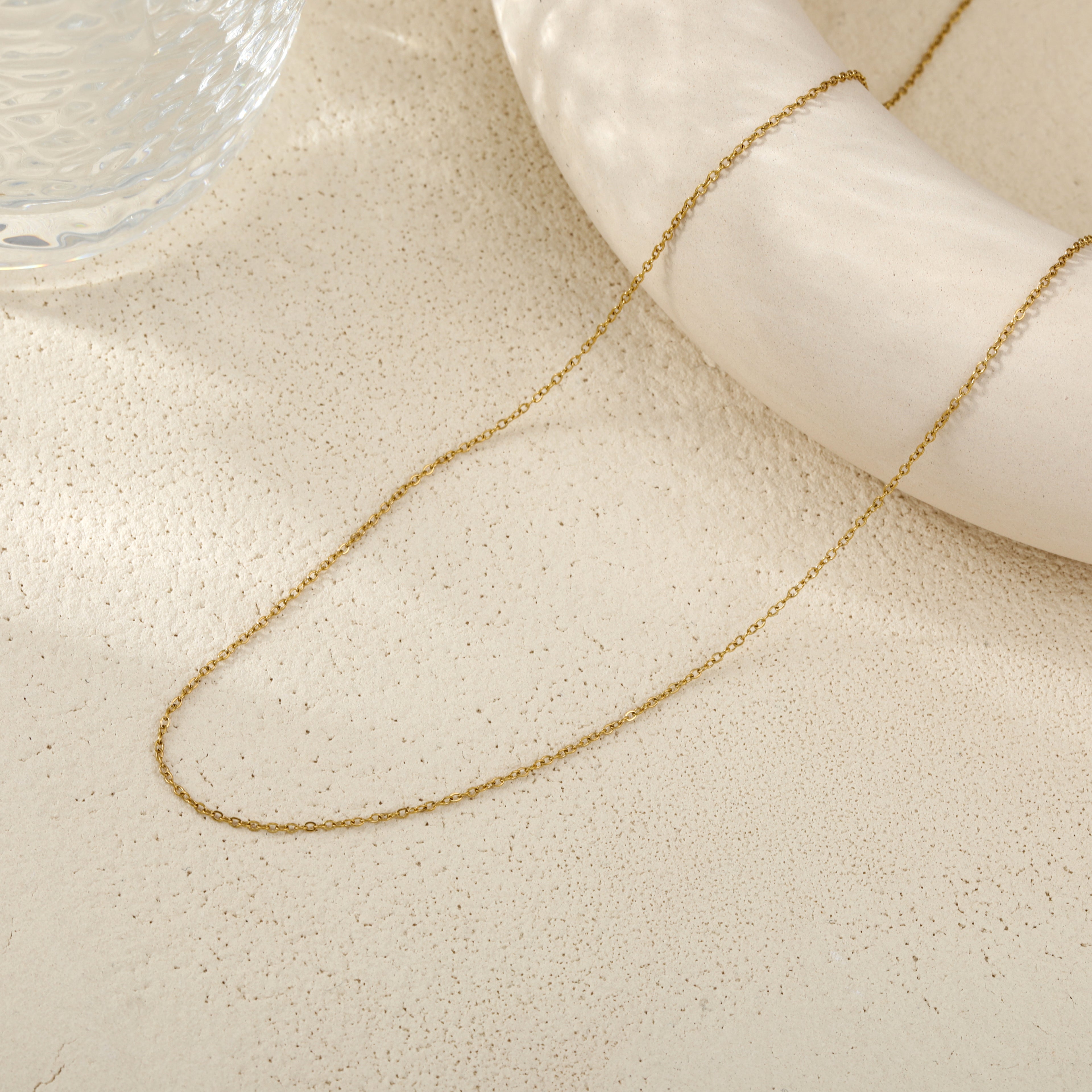 A delicate gold chain necklace draped over a white nautical-style ring prop on a textured beige surface.